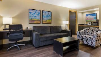 Quarto de hotel moderno com sofá, poltrona, escrivaninha e luminária.
