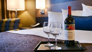 A hotel room with a bed, two bedside tables, a lamp, a phone, and a tray with a wine bottle and two glasses.