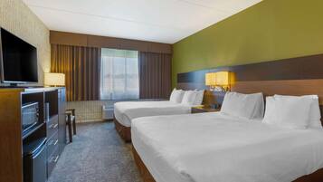 A hotel room with two beds, a TV, a desk, and a window with curtains.
