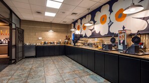 A buffet area with a counter, food display, and a wall with a floral mural.