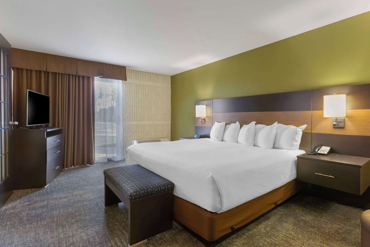 A hotel room with a large bed, bedside tables, a TV, and a window with curtains.