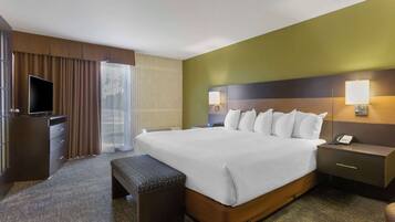 A hotel room with a large bed, bedside tables, a TV, and a window with curtains.