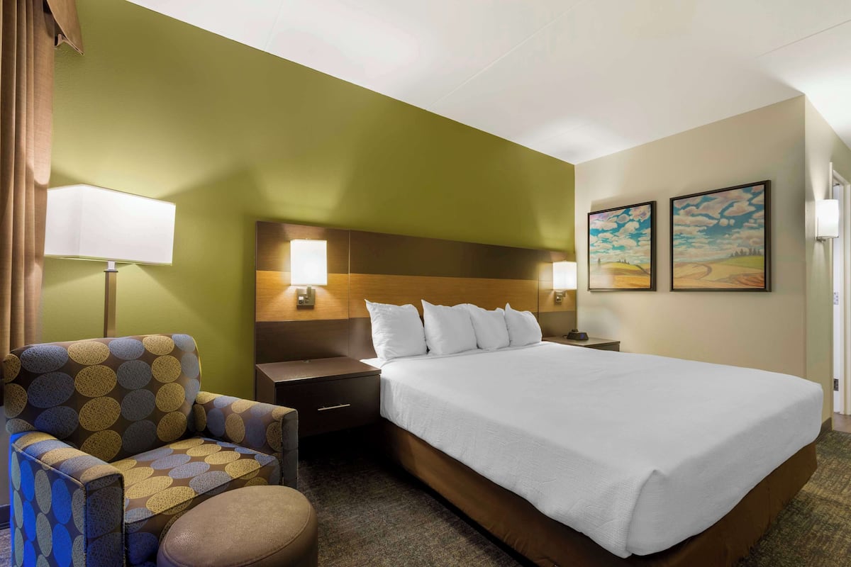 A hotel room with a large bed, a chair, a nightstand, and two wall-mounted lamps.