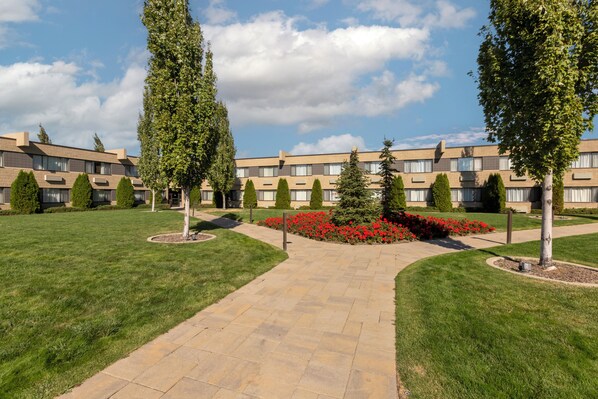 A courtyard with a paved walkway, surrounded by neatly trimmed grass and red flowers.