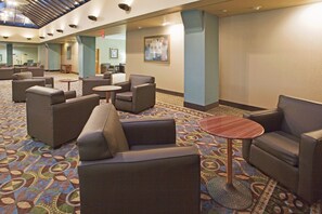 A hotel lobby with seating areas, a patterned carpet, and a ceiling with recessed lighting.