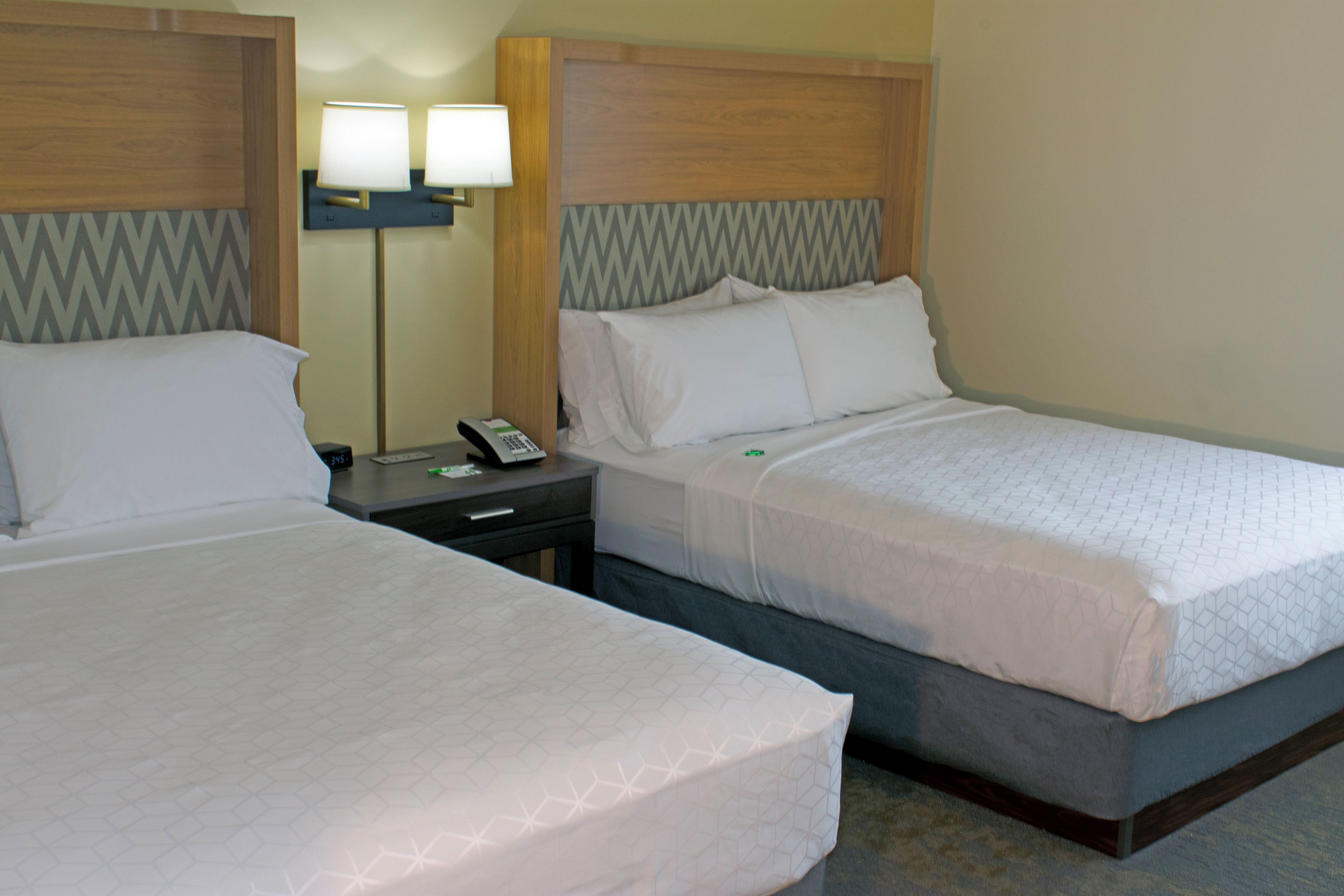 A hotel room with two beds, a nightstand with a lamp, and a wall clock.