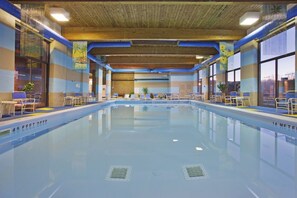 An indoor swimming pool with clear water, marked depth levels, and lounge chairs along the sides.