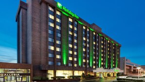 Un hôtel Holiday Inn avec une façade en briques, des éléments décoratifs verts illuminés et une entrée bien visible avec une enseigne.