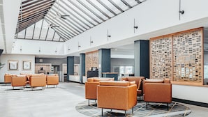 Un hall d’entrée spacieux avec un plafond haut, des sièges modernes et un grand écran en bois.