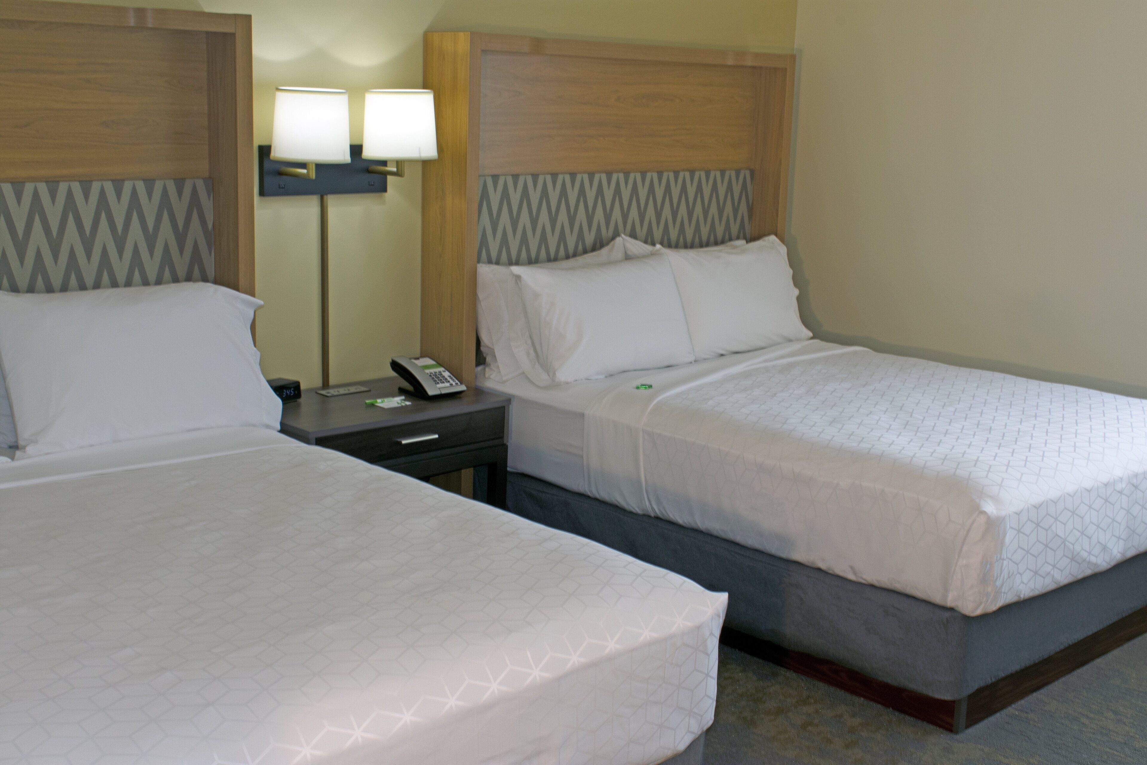 Two adjacent hotel beds with wooden headboards, a nightstand with a lamp, and a telephone.