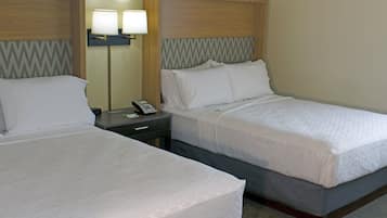 Two adjacent hotel beds with wooden headboards, a nightstand with a lamp, and a telephone.