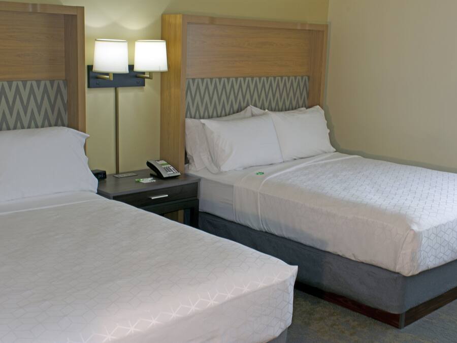Two adjacent hotel beds with wooden headboards, a nightstand with a lamp, and a telephone.