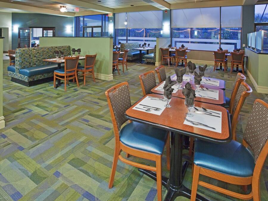 A dining area with tables set for four, chairs, and a patterned carpet.
