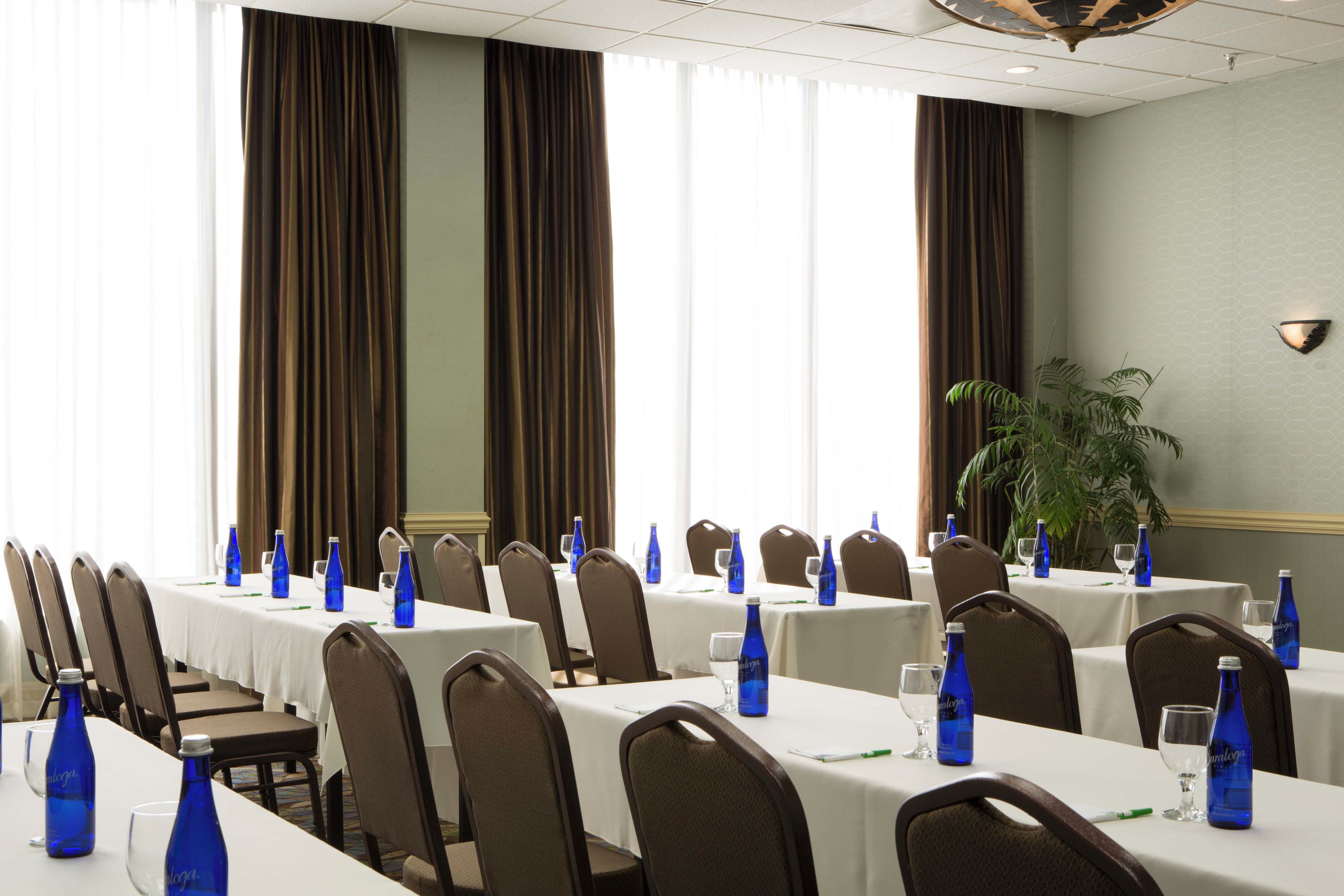 Un salón de conferencias con mesas dispuestas para reuniones, equipado con botellas de agua y vasos.