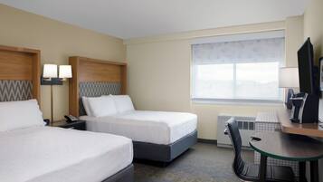A hotel room with two beds, a desk, a chair, a TV, and a window.