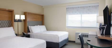 A hotel room with two beds, a desk, a chair, a TV, and a window.