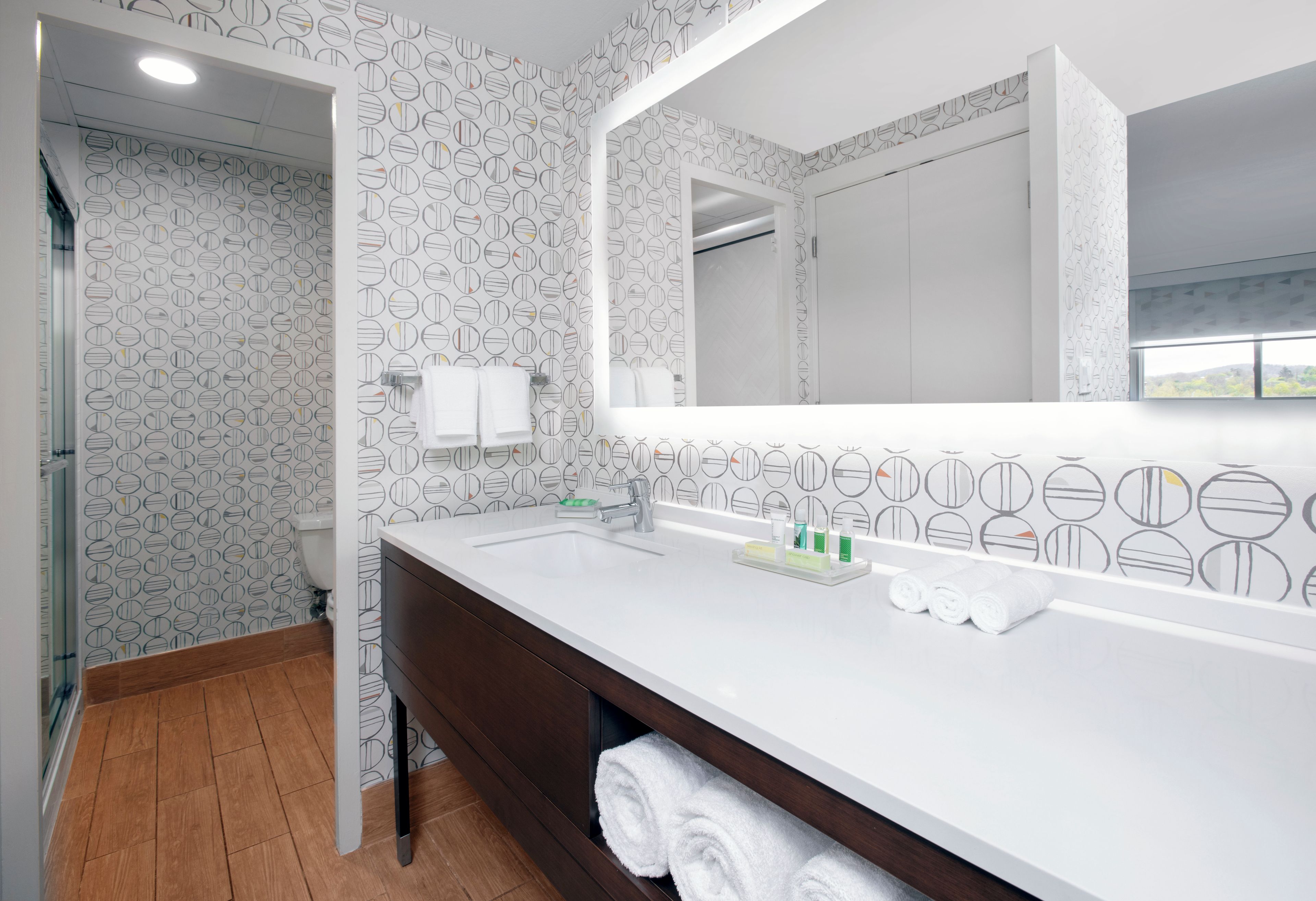 A modern bathroom with a white sink, a large mirror, and patterned wallpaper.