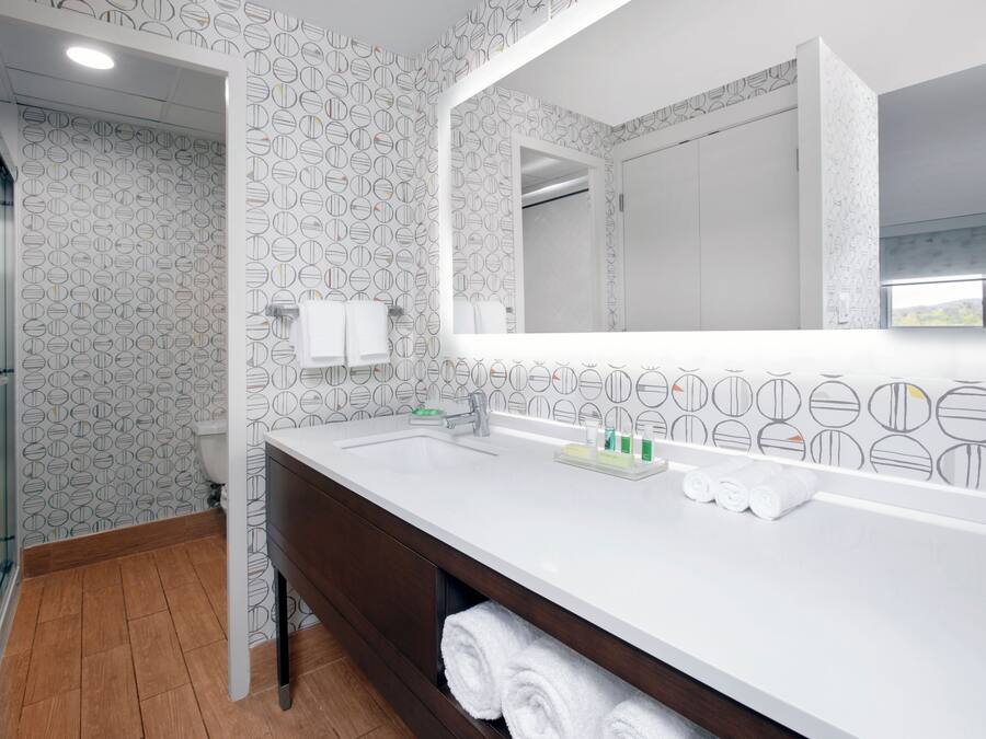 A modern bathroom with a white sink, a large mirror, and patterned wallpaper.