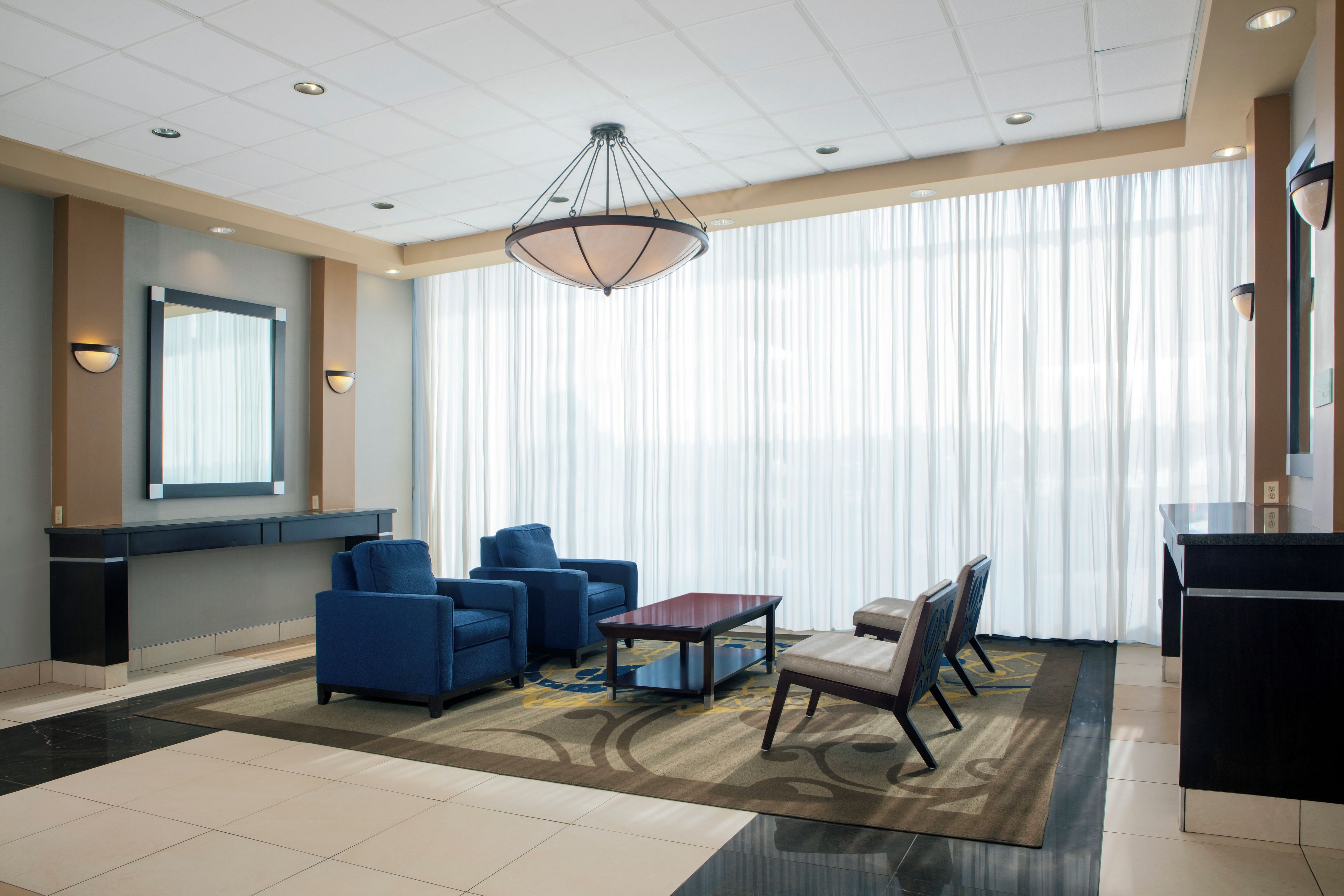 Un hall d’hôtel doté d’une grande fenêtre, d’un lustre et de différents espaces aménagés pour s’asseoir.