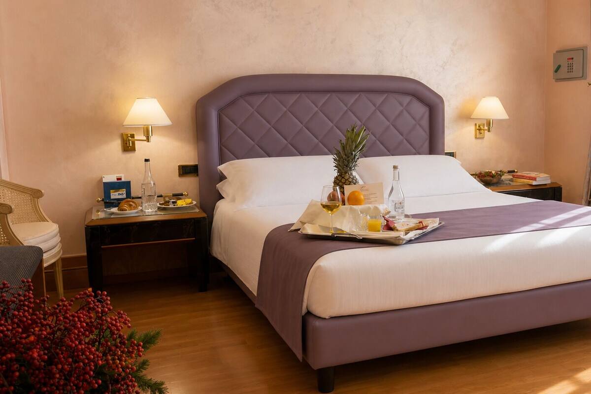 A neatly made bed with a tray of breakfast items, a nightstand with a lamp, and a chair.