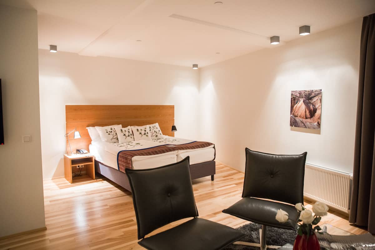 A hotel room with a bed, two chairs, a nightstand, a lamp, and a framed picture on the wall.