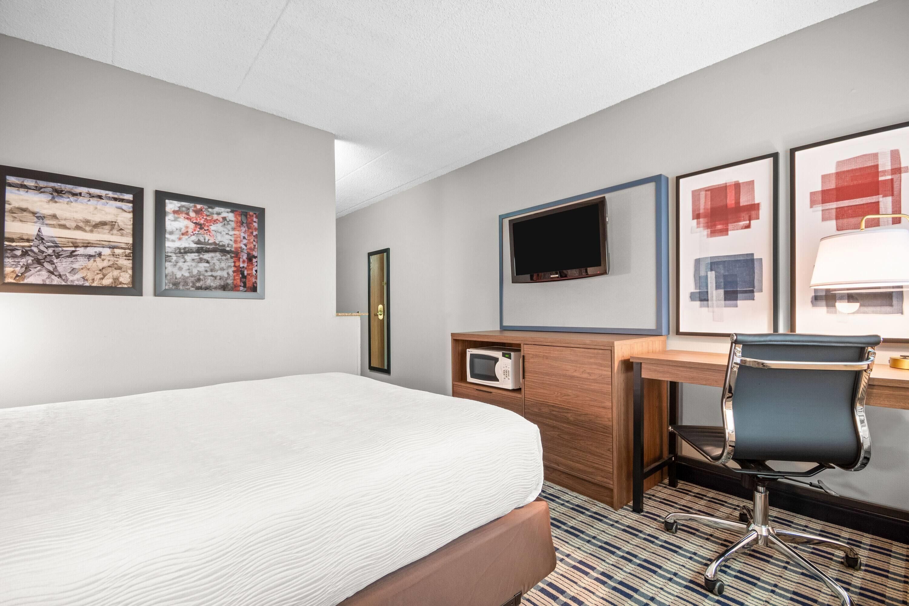Habitación de hotel con cama, escritorio, silla, televisor y obras de arte en las paredes.