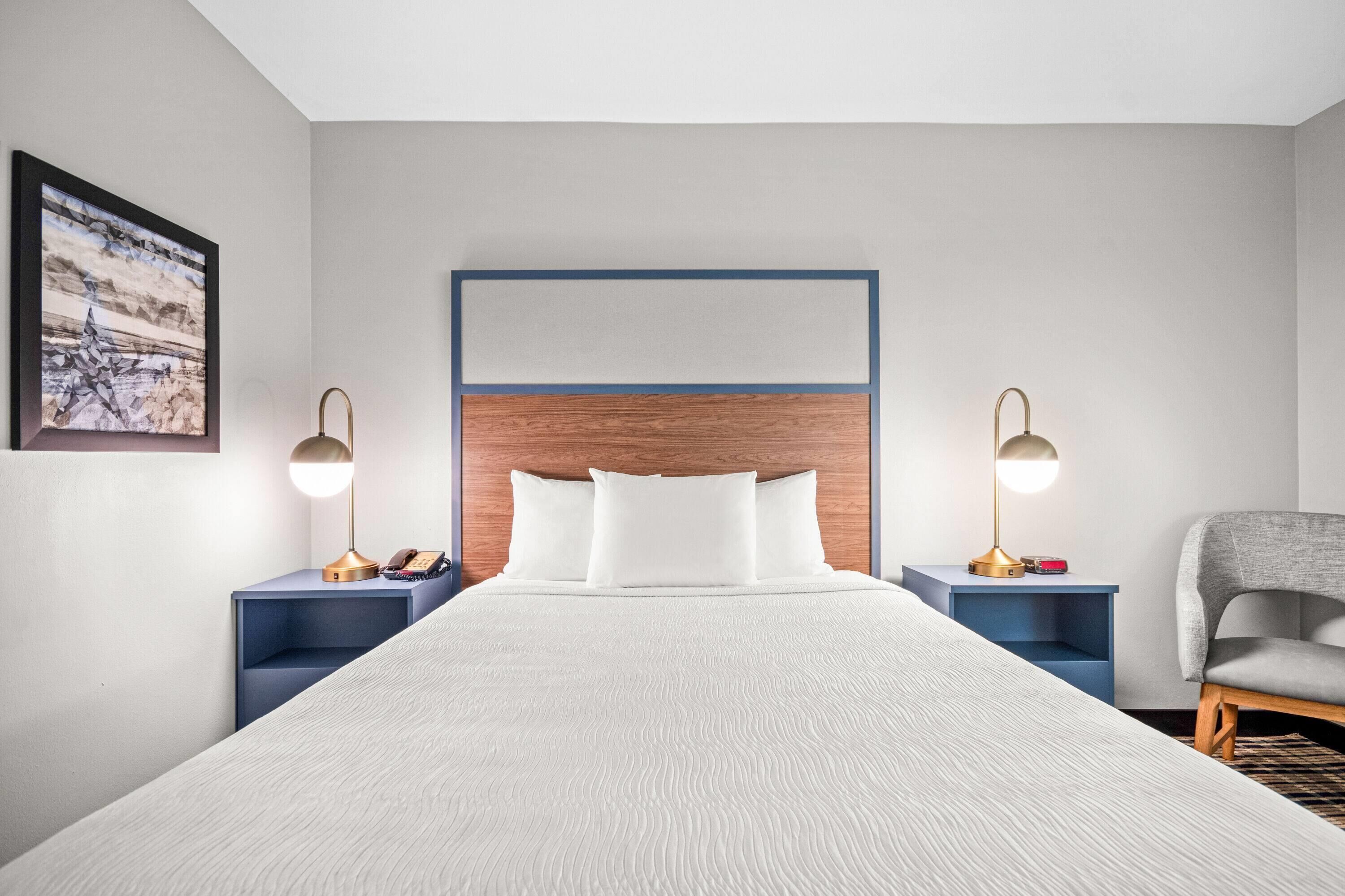 A hotel room with a large bed, two bedside tables with lamps, a chair, and a framed picture on the wall.