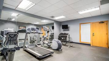 Un gimnasio con cintas de correr, elípticas y una pared de mancuernas.