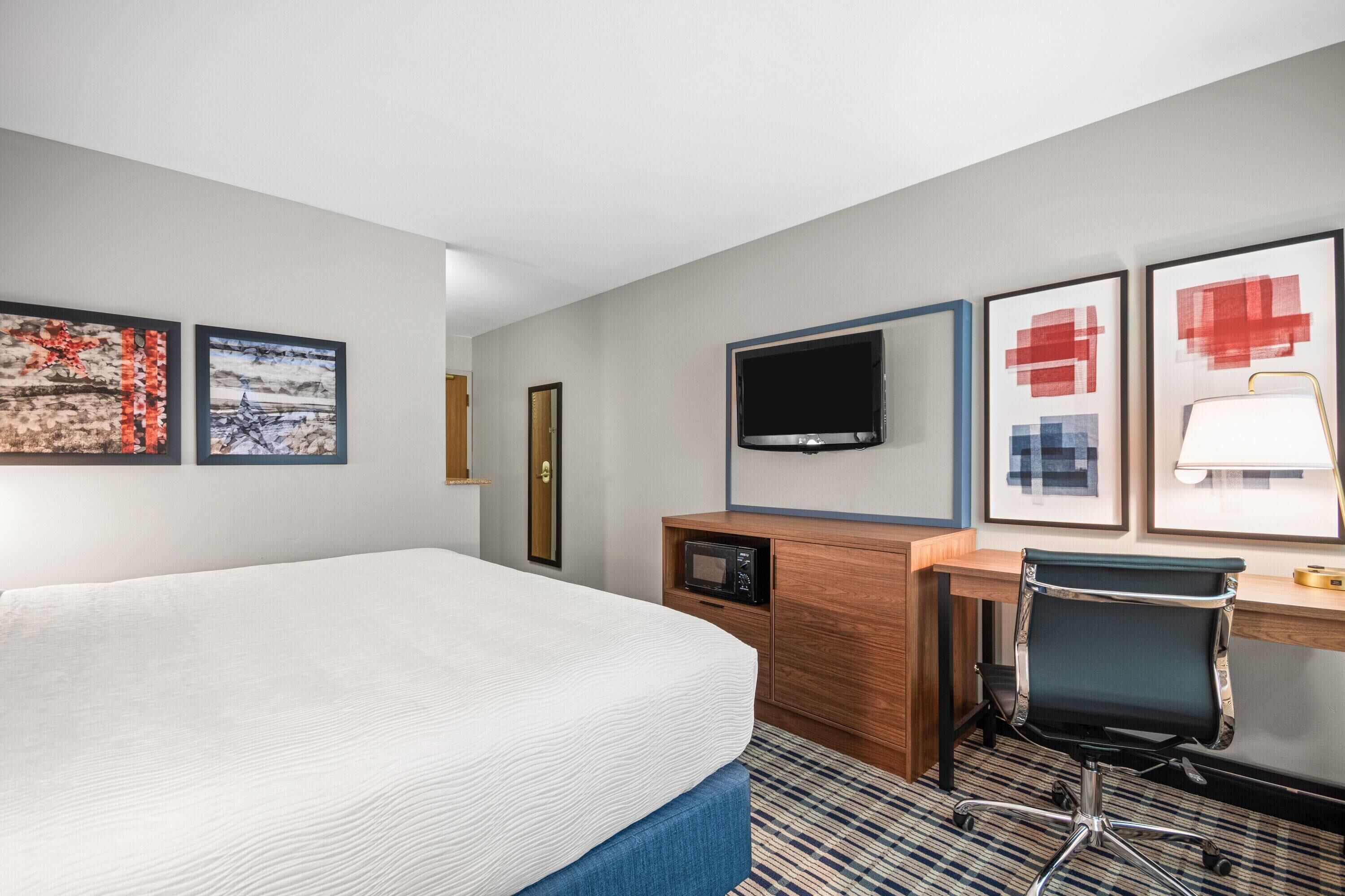 Habitación de hotel con cama, escritorio con computadora, televisión y cuadros en la pared.