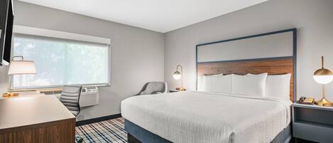 Habitación de hotel con una cama grande, un escritorio, una silla, un televisor y una ventana.
