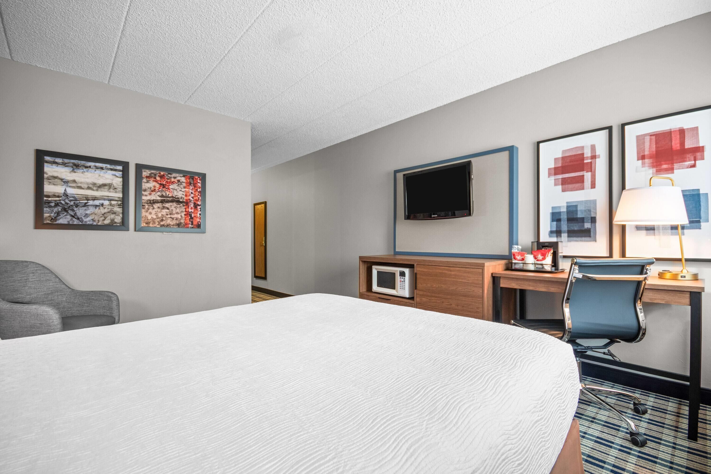Habitación de hotel con una cama grande, un escritorio con computadora, un televisor y dos cuadros en la pared.