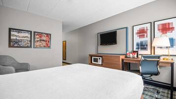Habitación de hotel con una cama grande, un escritorio con computadora, un televisor y dos cuadros en la pared.