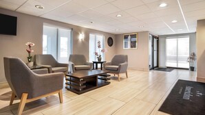 A modern waiting area with a reception desk, two armchairs, a coffee table, and a large window providing natural light.