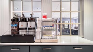 A coffee station with espresso machines, a coffee grinder, and a glass display case with cups and a red container.