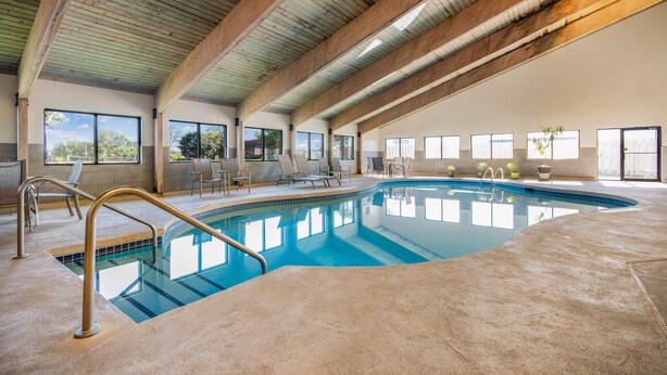 An indoor swimming pool with clear glass walls, wooden beams on the ceiling, and several lounge chairs around the pool.