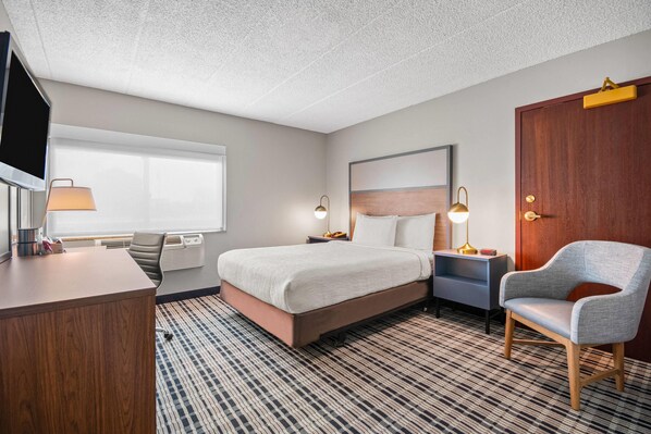 Une chambre d’hôtel comprenant un lit, un bureau, une chaise, une télévision, une fenêtre et une porte.