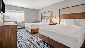 A hotel room with two beds, a desk, a chair, a TV, and a window with blinds.
