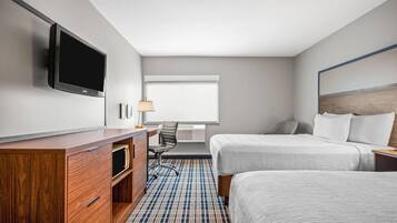 Une chambre d’hôtel équipée d’une télévision à écran plat, d’un bureau en bois, de deux lits, d’une lampe et d’une fenêtre avec des stores.