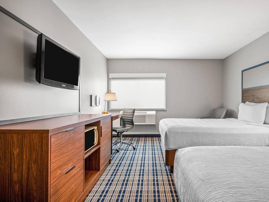 Une chambre d’hôtel équipée d’une télévision à écran plat, d’un bureau en bois, de deux lits, d’une lampe et d’une fenêtre avec des stores.