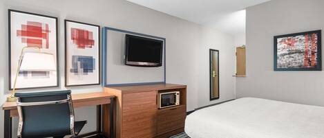 A hotel room with a bed, a desk with a chair, a television, and artwork on the walls.