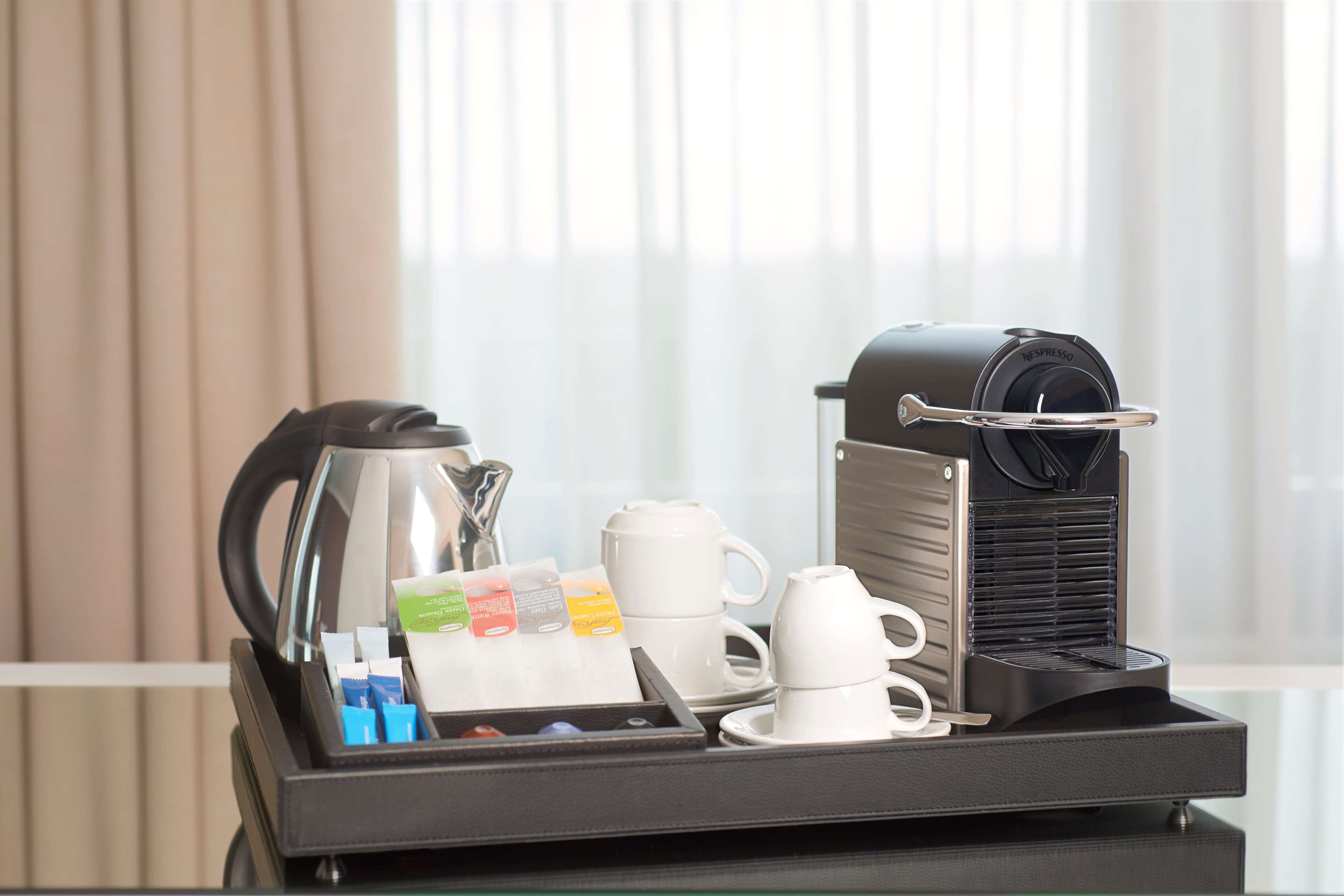 A coffee machine with a tray of coffee cups, a coffee pot, and coffee pods on a table.