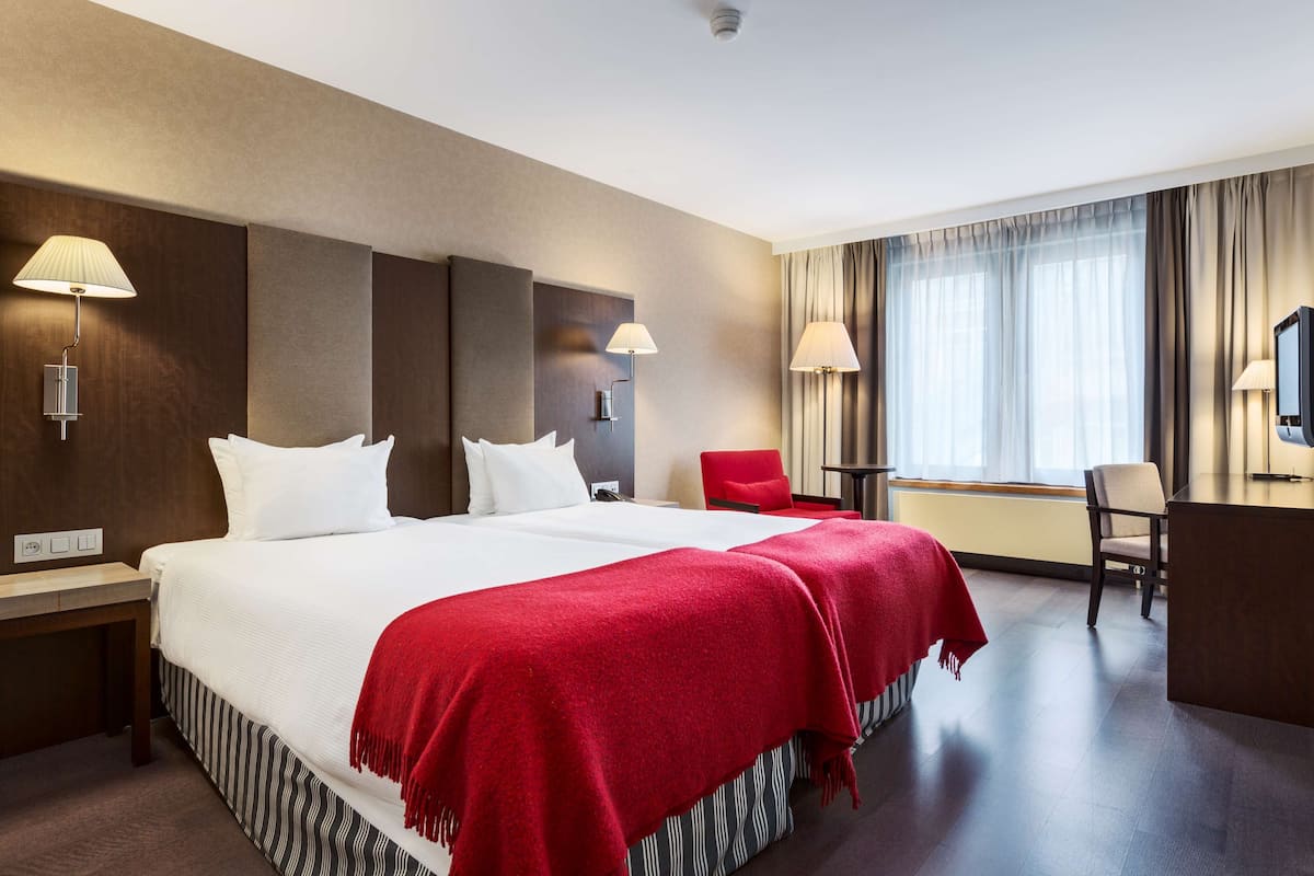 A hotel room with a large bed, two bedside tables, a desk, a chair, and a TV.