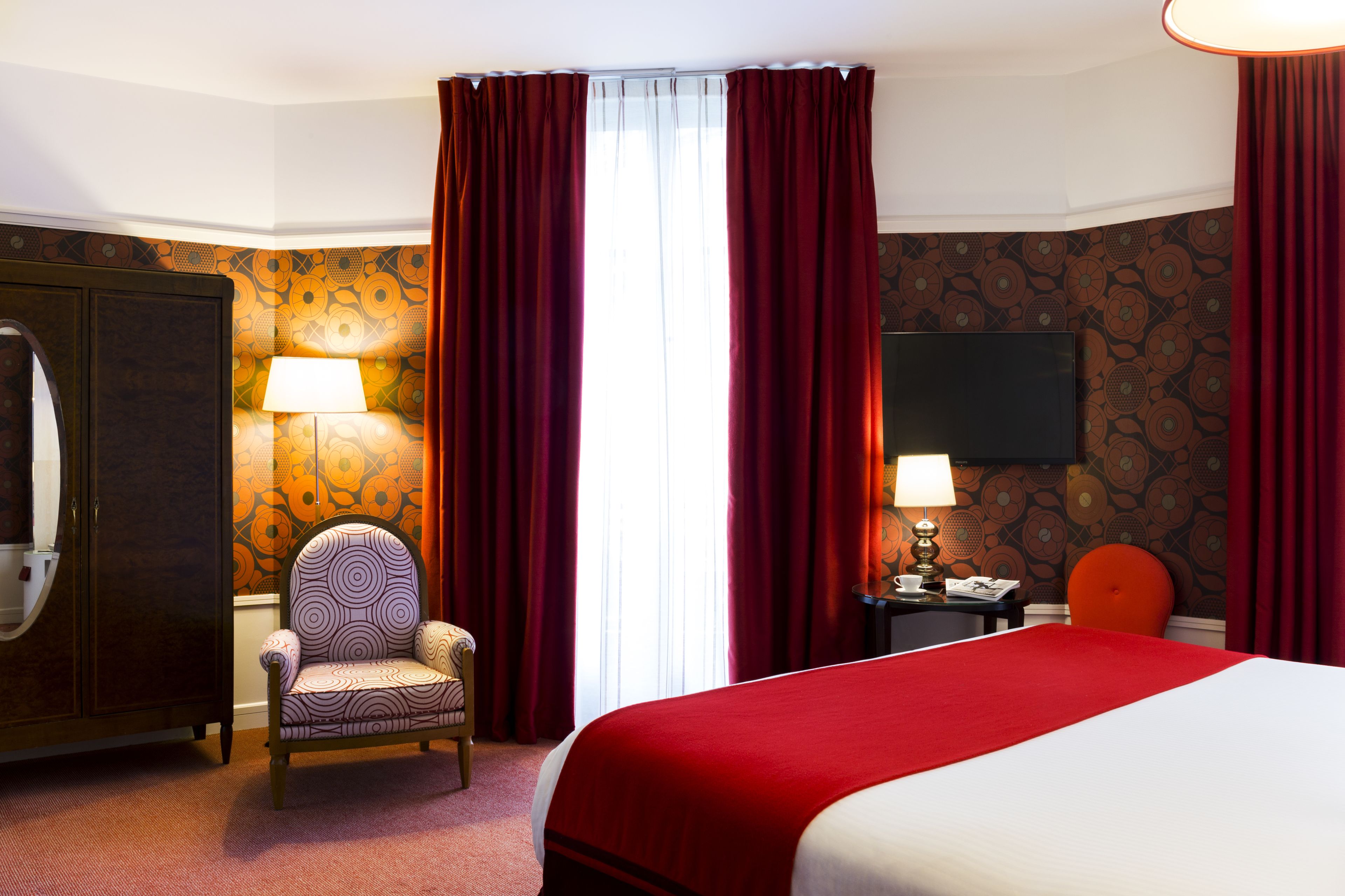 A hotel room with a bed, a chair, a desk, a lamp, and a television.