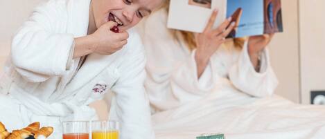 Una habitación de hotel con una cama, una bandeja con alimentos para el desayuno y una persona leyendo un libro.