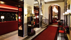 Et hotellobby med rød løber, en reception, en trappe og en lysekrone.