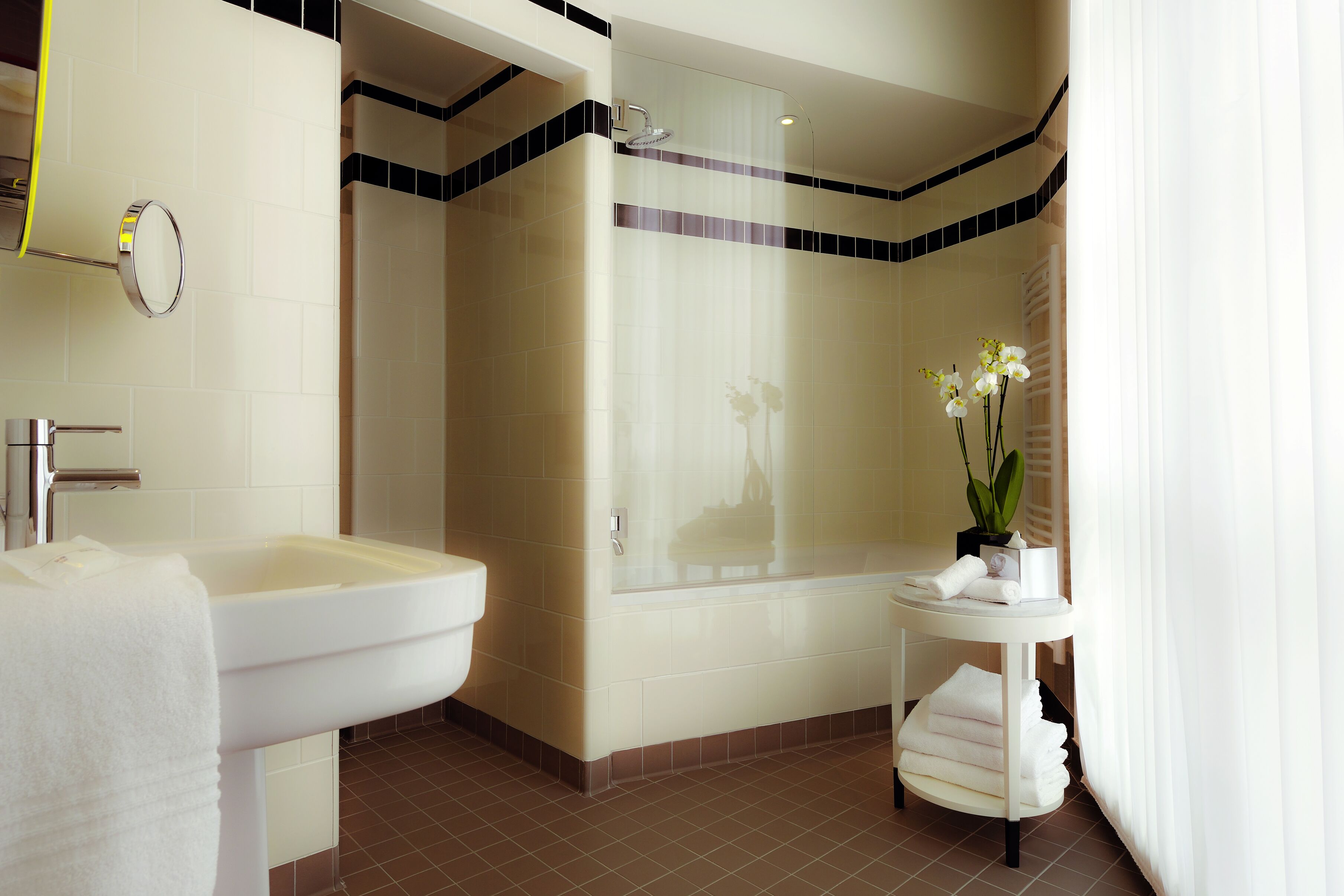 A modern bathroom with a sink, shower, and a small table with towels and a plant.