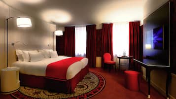 A hotel room with a large bed, a desk, a chair, a TV, and a red carpet.