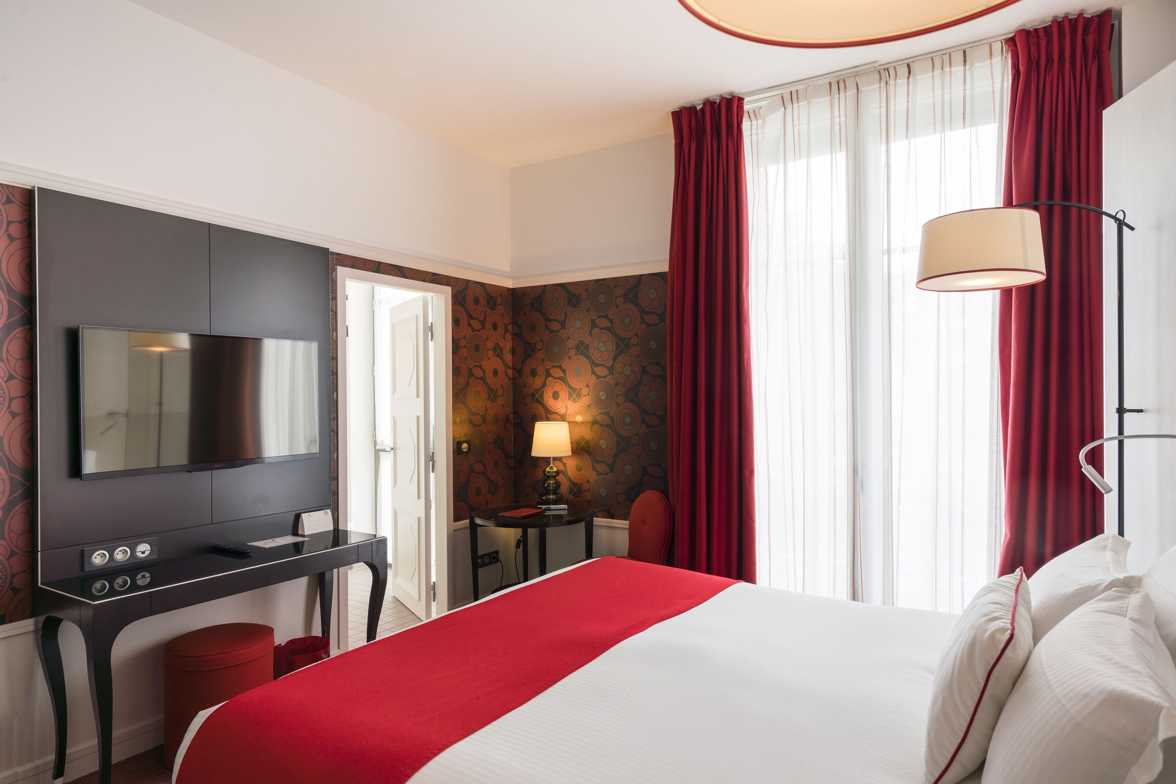 A hotel room with a large bed, a flat-screen TV, a desk, and a lamp.
