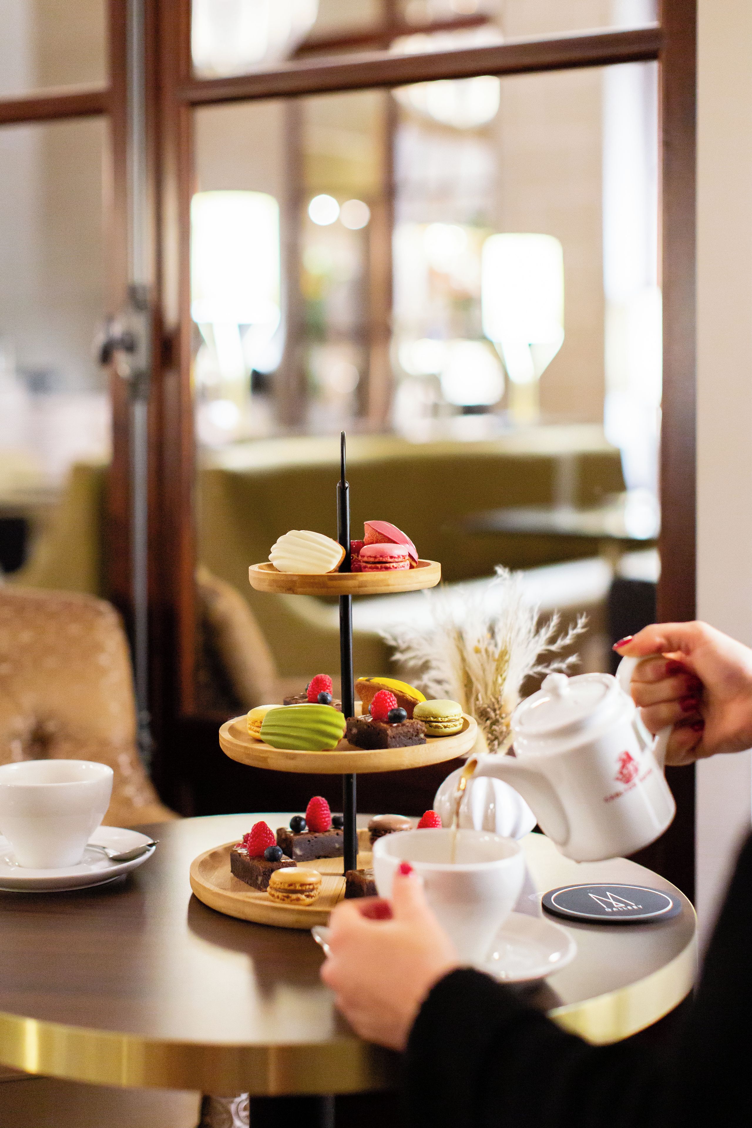 A three-tiered dessert stand with various pastries and fruits, a white cup, and a saucer on a table.