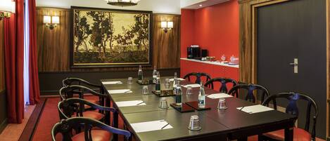 A conference room with a long table, chairs, a painting on the wall, and a coffee station.